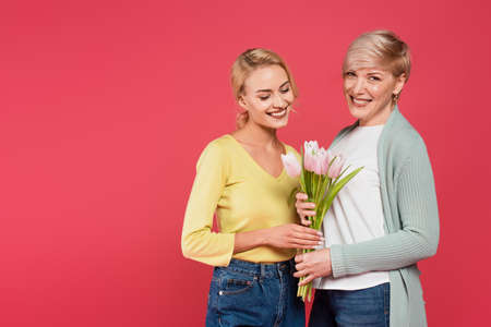 cheerful, stylish mother and daughter holding tulips isolated on pink
