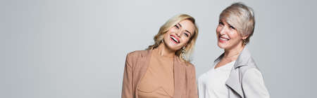 joyful mother and daughter in stylish outfit smiling at camera isolated on gray, banner