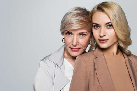 stylish, middle aged woman with adult daughter looking at camera isolated on gray