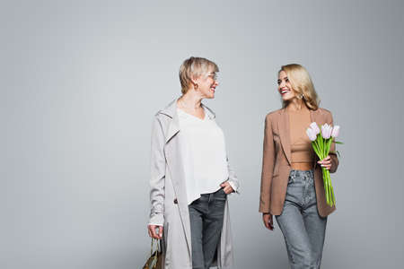 happy mother and daughter with shopping bag and tulips looking at each other on grayの写真素材