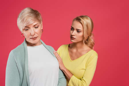 worried woman touching offended mother isolated on pinkの写真素材