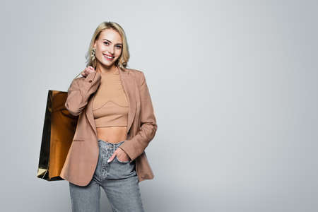 blonde woman with shopping bag standing with hand in pocket on grayの写真素材
