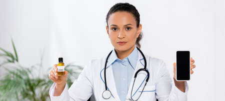 african american doctor holding bottle with cbd and smartphone with blank screen, bannerの写真素材