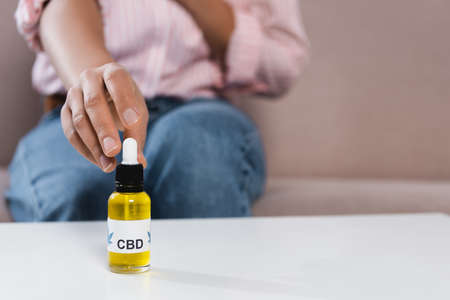 partial view of blurred african american woman reaching bottle with cbd letting on table