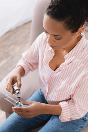 high angle view of brunette african american woman holding bottle with with dried medical cannabis...