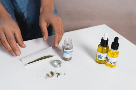 cropped view of african american woman reaching paper with dried medical cannabis near cbd bottlesの写真素材