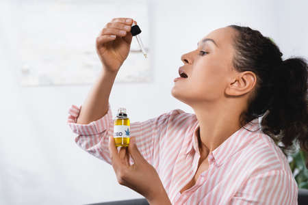 african american woman with open mouth holding bottle with cbd lettering and pipetteの写真素材