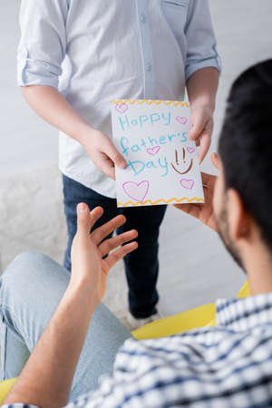 cropped view of boy holding happy fathers day card near dad on blurred foregroundの写真素材