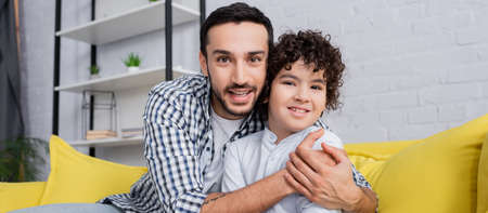joyful muslim man embracing happy son while looking at camera, banner