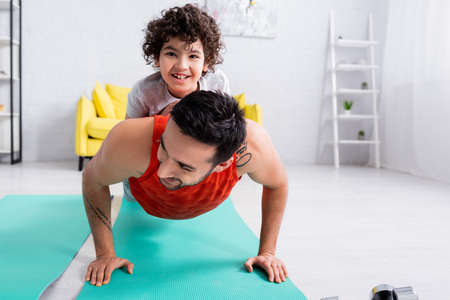 Happy arabian man doing press ups with son on fitness mat at homeの写真素材
