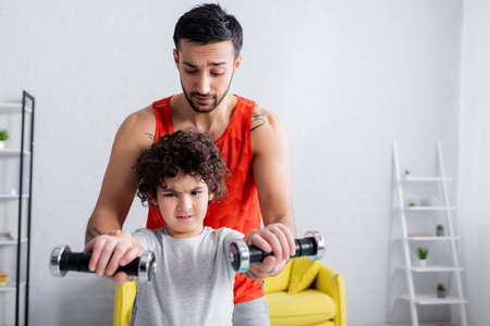 Concentrated arabian boy training with dumbbells near father at home