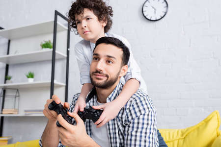 KYIV, UKRAINE - JANUARY 15, 2021: concentrated arabian boy playing video game together with skeptical fatherの写真素材