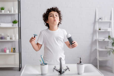 Arabian boy holding shaving foam and razor near sink in bathroom