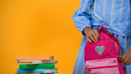 cropped view of schoolgirl holding backpack near books isolated on yellowの写真素材