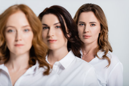 Woman in white shirt looking at camera near friends on blurred foreground isolated on grayの写真素材