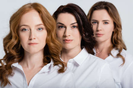 Brunette woman looking at camera near friends on blurred foreground isolated on grayの写真素材