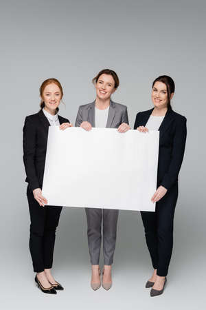 Cheerful businesswomen with white placard on gray backgroundの写真素材