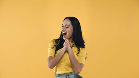 astonished woman with open mouth standing with clenched hands isolated on yellowの写真素材