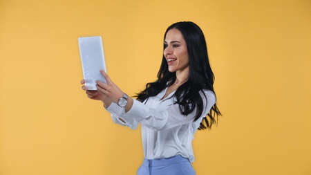 cheerful businesswoman taking selfie on digital tablet isolated on yellow