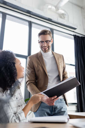 Smiling businessman holding paper folder near african american colleague on blurred foregroundの写真素材