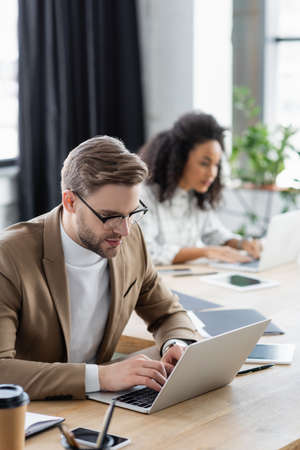 Businessman using laptop near gadgets on office tableの写真素材