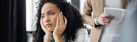 African american businesswoman looking away near colleague with digital tablet on blurred background, bannerの写真素材