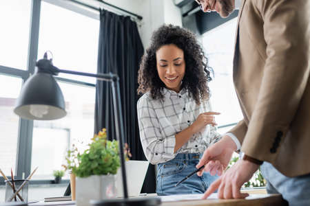 Smiling african american businesswoman looking at documents near businessman with pen in officeの写真素材