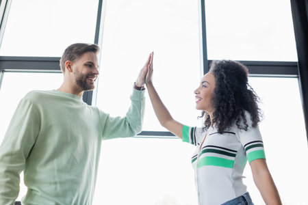 low angle view of young, successful interracial business colleagues giving high five in officeの写真素材