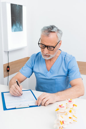 rehabilitologist writing prescription on clipboard near spine modelの写真素材