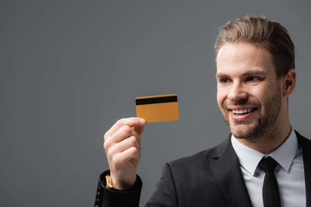 smiling businessman holding credit card isolated on grayの写真素材