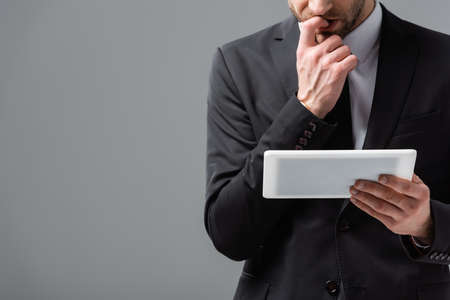 cropped view of worried businessman holding digital tablet isolated on gray