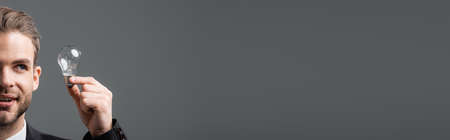 partial view of smiling businessman looking at light bulb isolated on gray, bannerの写真素材