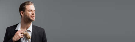 tense businessman with closed eyes touching rope on neck isolated on gray, bannerの写真素材