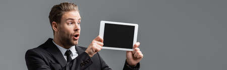 astonished manager holding digital tablet with blank screen isolated on gray, bannerの写真素材