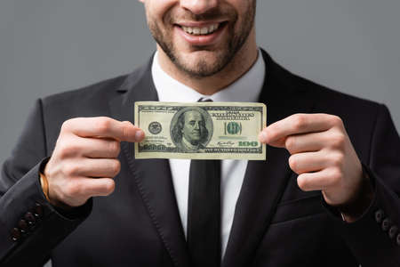 cropped view of smiling businessman holding dollar banknote isolated on gray, blurred backgroundの写真素材