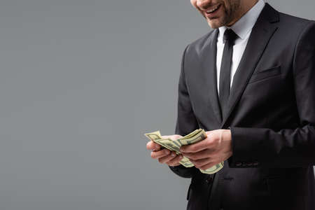 partial view of businessman in black suit counting dollars isolated on gray