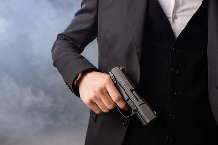 partial view of businessman with gun on gray background with smokeの写真素材