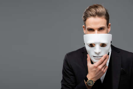 businessman holding mask near face while looking at camera isolated on grayの写真素材