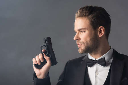 young, confident businessman holding weapon on gray background with smokeの写真素材