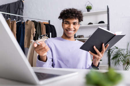 African american businessman holding pen and notebook near laptop on blurred foreground in showroomの写真素材