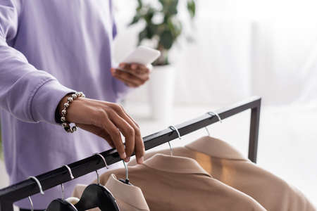 Cropped view of african american owner of showroom holding smartphone and standing near clothes on hangersの写真素材