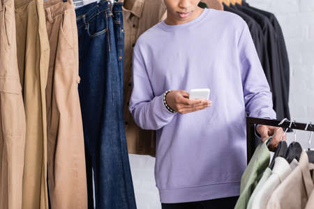 Cropped view of african american owner of showroom using smartphone near clothesの写真素材