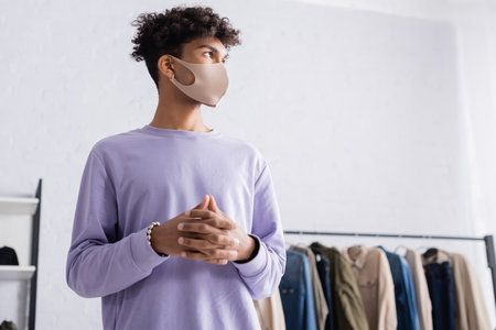 Low angle view of african american owner of showroom in protective mask looking awayの写真素材