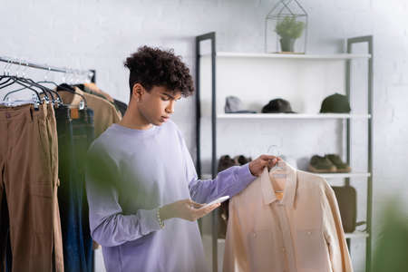 African american businessman using smartphone and holding shirt near clothes in showroomの写真素材