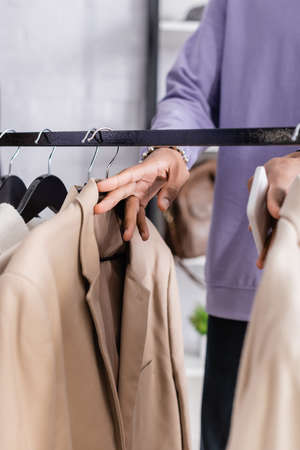 Cropped view of african american showroom owner holding smartphone near clothes on hangers