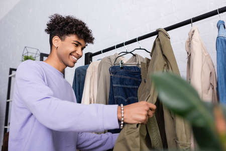 Cheerful african american showroom proprietor looking at clothes on hanging rackの写真素材