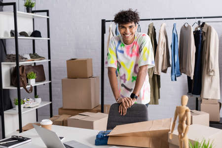 African american owner of showroom smiling at camera near shopping bag and box on tableの写真素材