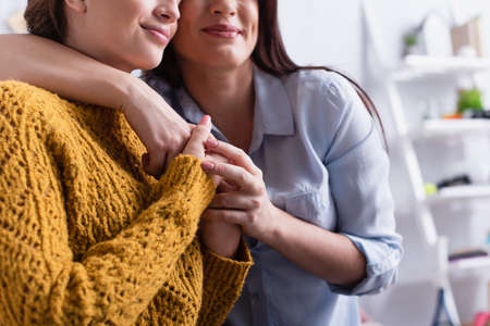 partial view of positive mother and teenage girl smiling and hugging at homeの写真素材
