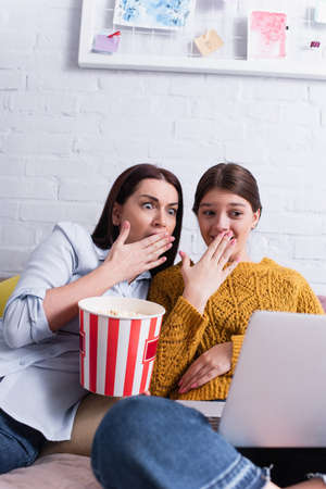 teenage girl and mother watching scary movie on laptop in bedroom