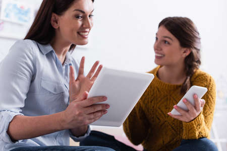 blurred teenage girl holding smartphone near happy mother with digital tabletの写真素材